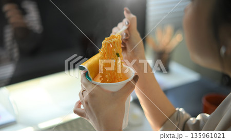 Closeup young woman eating instant noodles in office workplace Closeup young woman eating instant noodles in office workplace 135961021