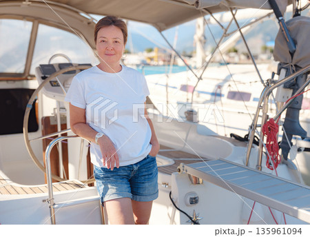 Mature woman relaxes on private yacht during sunny day in Finike Marina. Turkish coastline and luxury boats surround sailing vessel in Mediterranean port during summer vacation. Mature woman relaxes on private yacht during sunny day in Finike Marina. Turkish coastline and luxury boats surround sailing vessel in Mediterranean port during summer vacation. 135961094