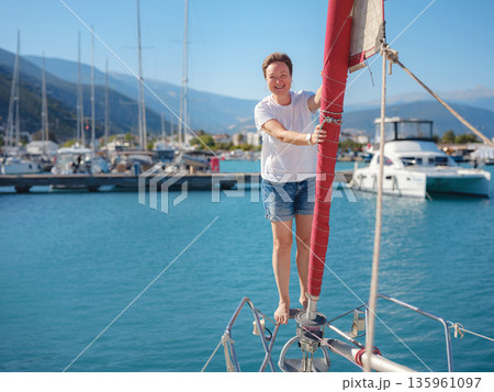Female sailor holds white sail cloth preparing to hoist sails on yacht. Physical activity and boat handling skills are shown during preparation for sailing trip near Finike coast. Female sailor holds white sail cloth preparing to hoist sails on yacht. Physical activity and boat handling skills are shown during preparation for sailing trip near Finike coast. 135961097