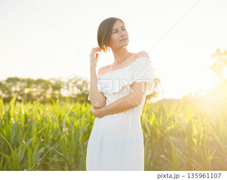 Beautiful woman in white dress standing in summer field during golden sunset in Croatia, warm sunlight, romantic evening mood, natural countryside atmosphere, soft wind and peaceful scene Beautiful woman in white dress standing in summer field during golden sunset in Croatia, warm sunlight, romantic evening mood, natural countryside atmosphere, soft wind and peaceful scene 135961107