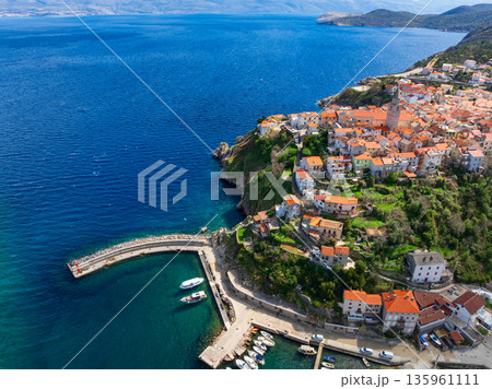 Drone captures stunning top view of Vrbnik towns on Krk Island in Croatia. Blue Adriatic Sea meets rocky coastline and traditional Mediterranean architecture from above. 135961111