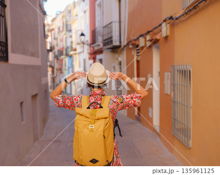 Woman in dress strolls through colorful streets of Spanish coastal town of La Vila Joiosa . sunny winter atmosphere highlights charm of Mediterranean architecture and quiet seaside life, back view 135961125