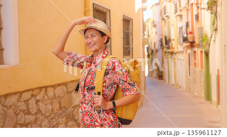 Woman in dress strolls through colorful streets of Spanish coastal town of La Vila Joiosa or Villajoyosa. sunny winter atmosphere highlights charm of Mediterranean architecture and quiet seaside life 135961127