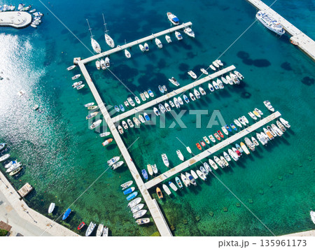 Drone captures stunning top view of Baska towns on Krk Island in Croatia. Blue Adriatic Sea meets rocky coastline and traditional Mediterranean architecture from above. 135961173
