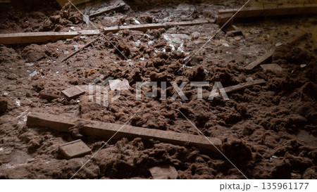 Dust covers the floor where wooden beams lie scattered among debris in a neglected building with light filtering through gaps, revealing a disordered space. 135961177
