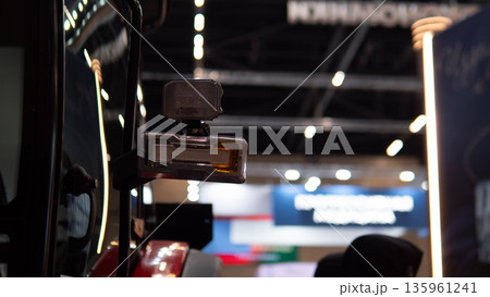 closeup robotic arm assembling components in trade show environment with blurred booths, metal grippers, exposed cables, precision servos and connectors, industrial lighting and showcase 135961241