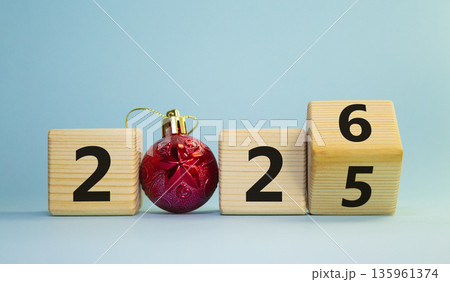 2026 New Year symbol. Businessman turns wooden cube and changes Year 2025 to 2026. Beautiful light blue background with Christmas ball. Copy space. Business and 2026 happy new year concept 135961374