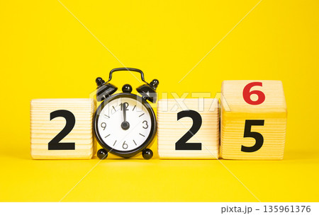 2026 New Year symbol. Businessman turns wooden cube and changes Year 2025 to 2026. Beautiful yellow background with Alarm clock. Copy space. Business and 2026 happy new year concept 135961376