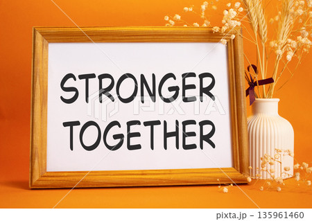 Stronger together symbol. Concept words Stronger together on beautiful wooden picture frame. Beautiful orange background with flower vase. Business and Stronger together concept. Copy space. 135961460