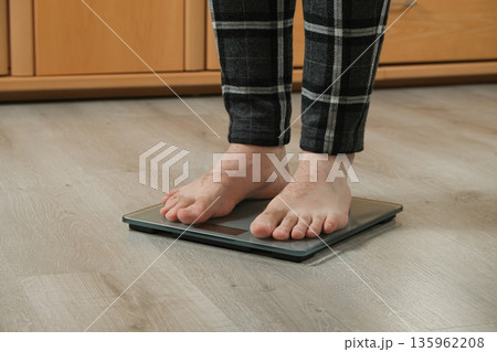 Man weighing himself on modern weighing scales at home, close-up of bare feet. Man weighing himself on modern weighing scales at home, close-up of bare feet. 135962208