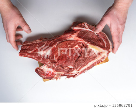 Top view of male hands holding a large raw beef steak. Fresh ribeye meat with bone isolated on white background. Copy space Top view of male hands holding a large raw beef steak. Fresh ribeye meat with bone isolated on white background. Copy space 135962791