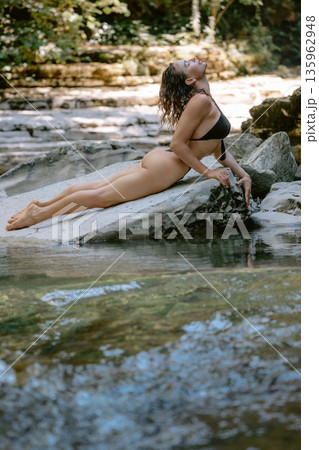 Attractive slim woman in bikini posing on rock river. 135962948