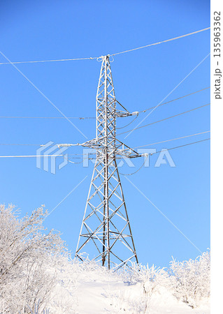 Winter landscape of Central Russia with an icy high-voltage power line. Beautiful trees covered in a thick layer of frost and snow in the bitter cold. A wonderful winter invitation card for tourists. Winter landscape of Central Russia with an icy high-voltage power line. Beautiful trees covered in a thick layer of frost and snow in the bitter cold. A wonderful winter invitation card for tourists. 135963362