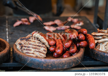 Grilled sausages and meat patties at food stand. Sausages and meat patties displayed on grill at a food stand. Concept of street food, catering, meal preparation 135963378