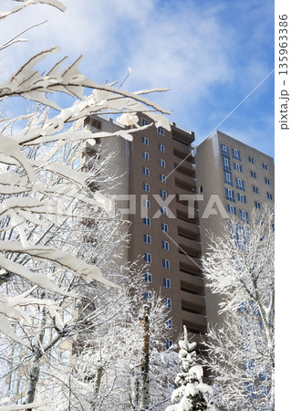 A multi-story building against a blue sky with snow-covered tree branches. 135963386