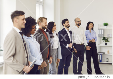 Young business people standing in a row on meeting in office listening to their colleague Young business people standing in a row on meeting in office listening to their colleague 135963619