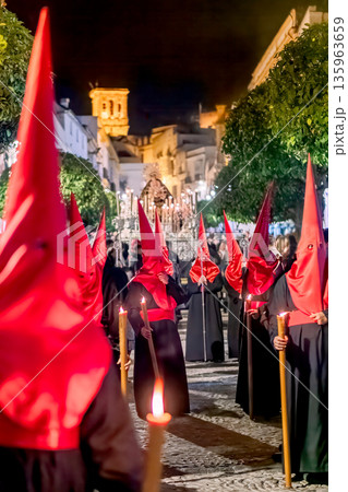 Many nazarenos with red hoods walking in procession 135963659