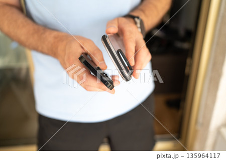 Close-up of a man holding a smartphone and a transparent protective case, preparing to put the case on the phone. Close-up of a man holding a smartphone and a transparent protective case, preparing to put the case on the phone. 135964117