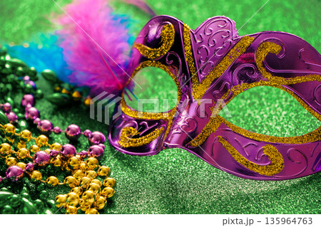 Carnival mask and colorful beads on green shiny background. Mardi Gras concept. Fat Tuesday symbol. 135964763
