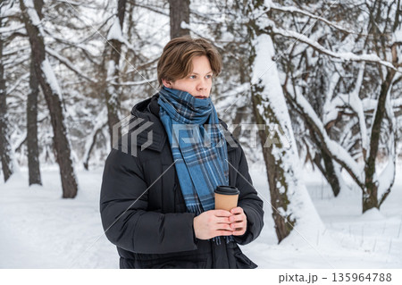 Young man holding hot coffee in snowy forest Young man holding hot coffee in snowy forest 135964788