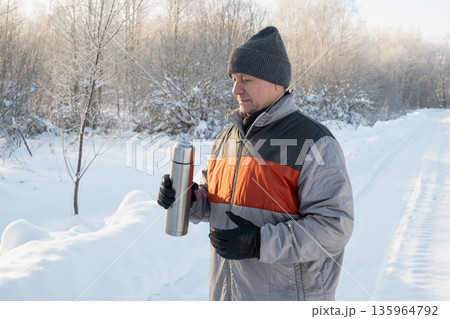 Mature man holding thermos outdoors in winter Mature man holding thermos outdoors in winter 135964792