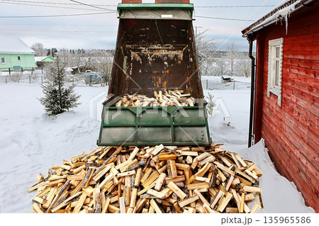 Delivery of split logs to house with wood stove heating, dump truck emptied bed unloading logs onto snow. 135965586