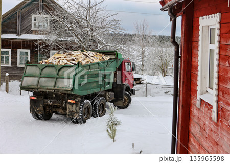 Firewood delivery truck turns onto driveway of rural house in snowy winter village. 135965598
