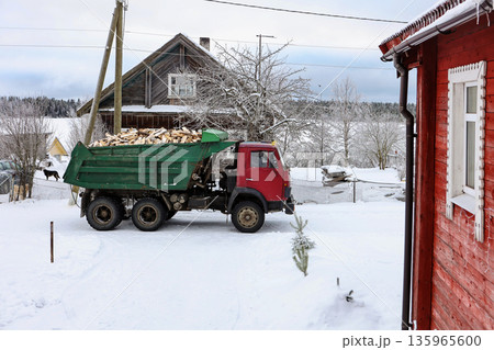 Dump truck with full load of firewood stands in snowy village in winter. Dump truck with full load of firewood stands in snowy village in winter. 135965600
