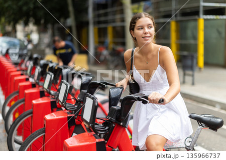 Young girl taking red bicycle from Bicing rental station Young girl taking red bicycle from Bicing rental station 135966737
