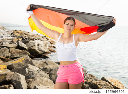 Young woman on coast posing with flag of Germany 135966803