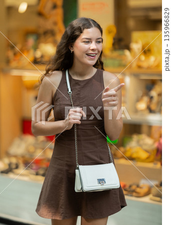 Beautiful young girl customer choosing something in souvenir shop during tourist trip in Spain 135966829