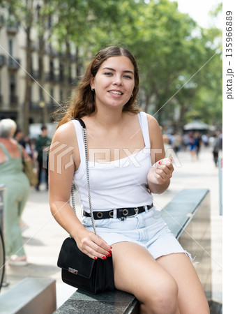 Happy young woman sitting on bench in Rambla Street of Barcelona 135966889