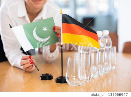 Preparing for business negotiations - woman sets small flags of countries of Germany and Pakistan on table Preparing for business negotiations - woman sets small flags of countries of Germany and Pakistan on table 135966947