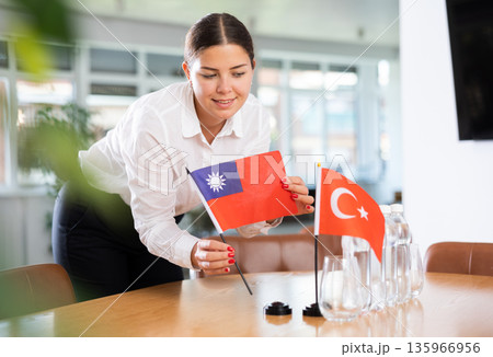 Positive young woman putting little flag of Taiwan on table next to the flag of Turkey Positive young woman putting little flag of Taiwan on table next to the flag of Turkey 135966956