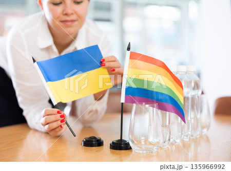 Young woman puts flags of Ukraine and LGBT on table in office Young woman puts flags of Ukraine and LGBT on table in office 135966992