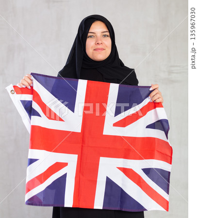 Balanced Muslim woman in traditional black hijab holds flag of Great Britain Balanced Muslim woman in traditional black hijab holds flag of Great Britain 135967030