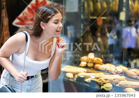 Smiling girl choosing bocadillos in glass showcase of spanish street cafe Smiling girl choosing bocadillos in glass showcase of spanish street cafe 135967043
