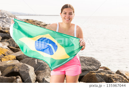 Pretty smiling girl holding Brazilian flag on the seashore on a sunny day Pretty smiling girl holding Brazilian flag on the seashore on a sunny day 135967044