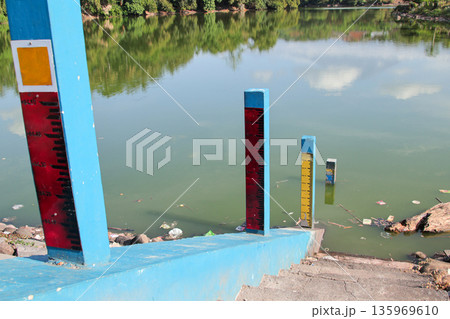 Water Level Markers Near Lake Indicating Flood Risk with Natural Light and Reflection, Promoting Environmental Awareness and Safety Measures Water Level Markers Near Lake Indicating Flood Risk with Natural Light and Reflection, Promoting Environmental Awareness and Safety Measures 135969610