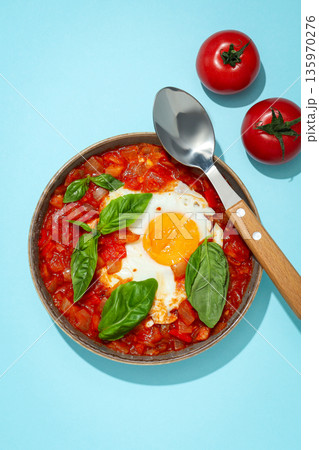 Eggs cooked in tomato sauce sit in a bowl with fresh basil 135970276