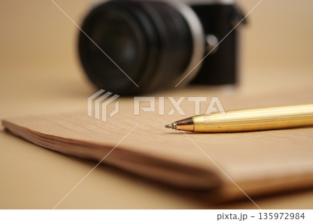 Camera and pen on desk with notebook close by Camera and pen on desk with notebook close by 135972984