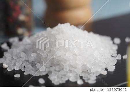 Salt sits on a black surface near spices and a container 135973041