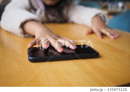 Child reaches for smartphone on wooden table Child reaches for smartphone on wooden table 135973128