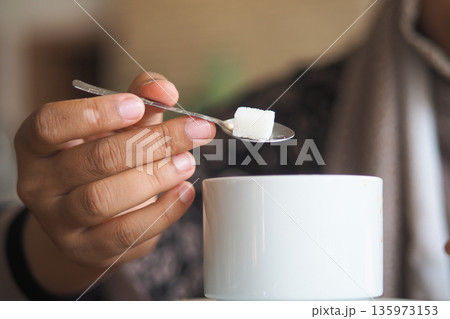 Adding sugar to cup of coffee in a cozy cafe setting 135973153