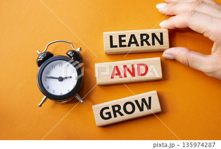 Learn and grow symbol. Concept words Learn and grow on wooden blocks. Businessman hand. Beautiful orange background with alarm clock. Business and Learn and grow concept. Copy space. 135974287