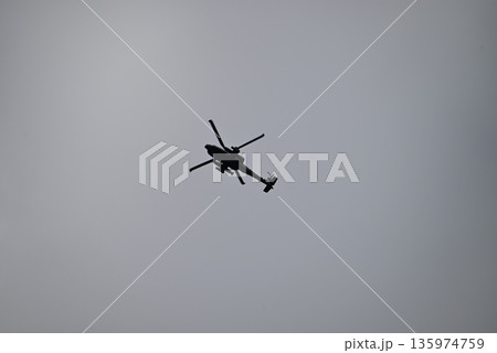 曇天の空を高く飛行するヘリコプターの黒いシルエット 135974759
