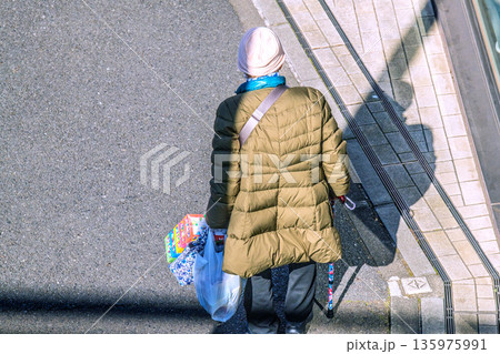 日本の横浜都市景観光と“陰”…高齢化社会　杖の高齢女性（マスク姿）。買い物帰り、左手は手袋… 135975991