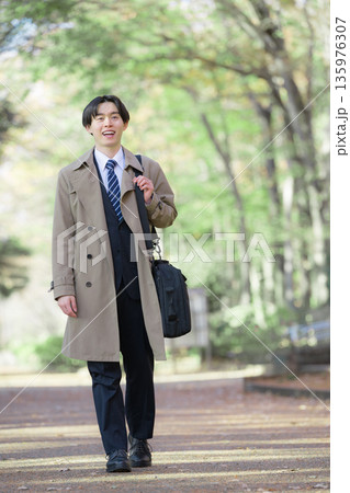 新緑背景で就活や新卒の笑顔のビジネスマン　外回りの営業で歩く	 135976307