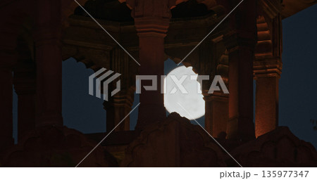 Full moon framed by arches of illuminated watchtower at Red Fort Delhi night scene 135977347