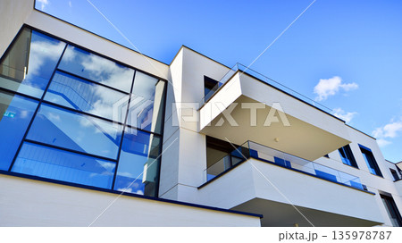 Modern architecture of urban residential apartment buildings on a sunny day. Low-rise apartment buildings with large windows and extensive terraces. White facade of a modern apartment building. Modern architecture of urban residential apartment buildings on a sunny day. Low-rise apartment buildings with large windows and extensive terraces. White facade of a modern apartment building. 135978787